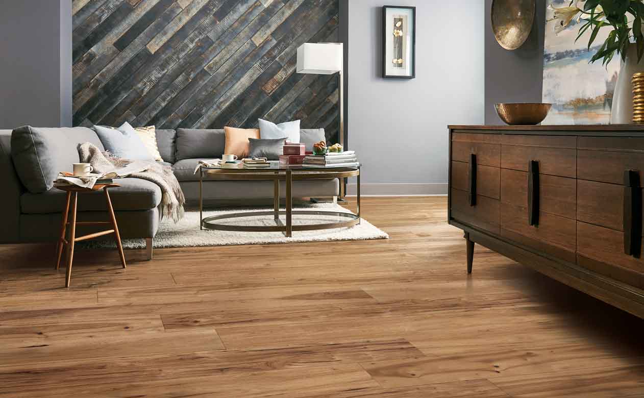 Modern living room with hardwood floors, a light shag area rug, gray sectional sofa, colorful pillows, glass coffee table, and dark wood side table, creating a cozy and stylish atmosphere.